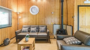 A cozy room with wooden walls, a sofa, a coffee table, a clock, and a fireplace.