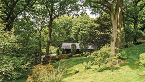 A serene garden with a small house surrounded by trees and grass.
