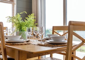 A wooden dining table set with white plates, bowls, and wine glasses, accompanied by a green plant in a white vase. - Luxurious lodge with vaulted ceilings and a welcoming feature fireplace. (Glastonbury)