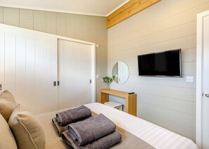 A bedroom with a bed, a TV, a mirror, a bedside table, and a wardrobe.