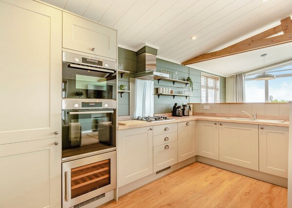 Une cuisine moderne avec des meubles blancs, un four encastré, un plan de travail en bois et une fenêtre qui laisse entrer la lumière naturelle.