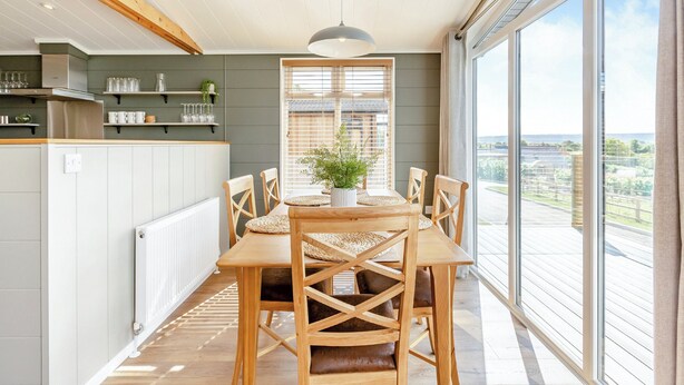 Eine moderne Küche mit Holzbalken, einem Essbereich mit Tisch und Stühlen sowie großen Fenstern mit Blick.