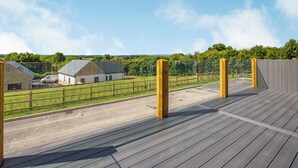 Eine Holzterrasse mit Blick auf eine ländliche Landschaft, darunter ein Bauernhof und ein Zaun.