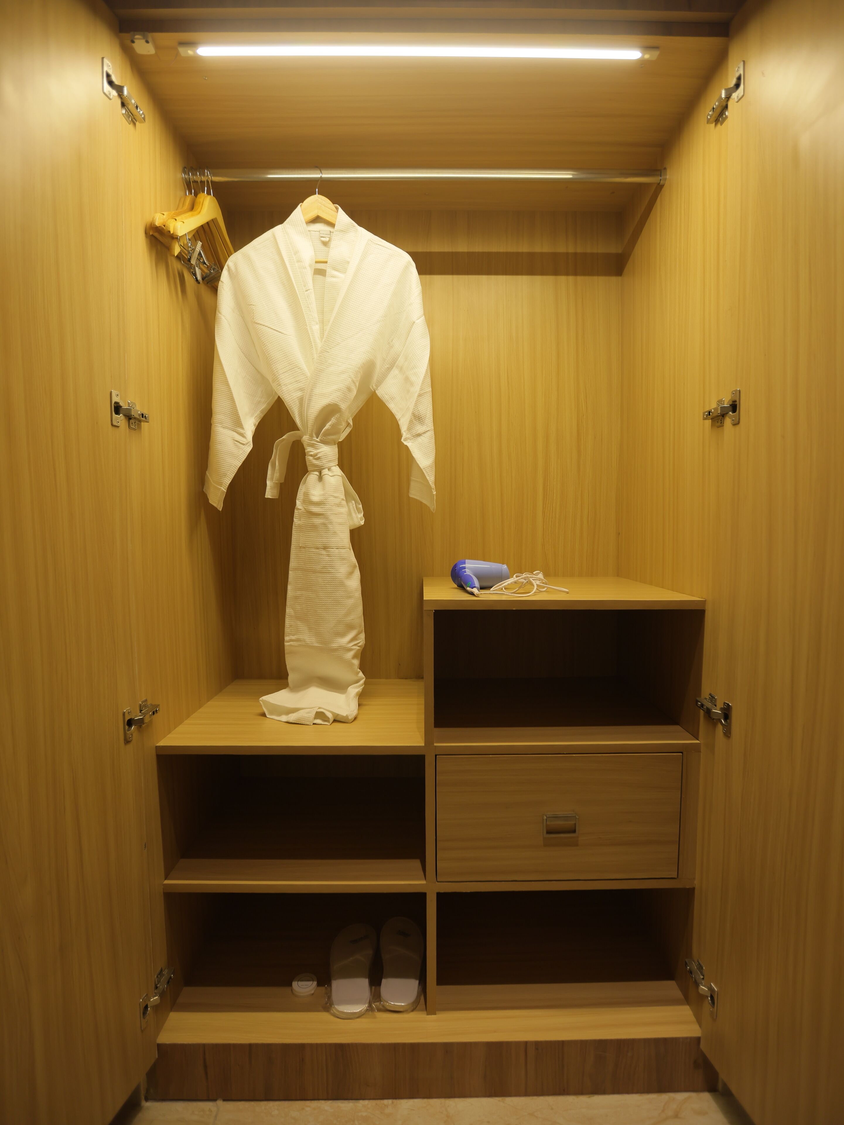 A walk-in closet with wooden doors, a robe hanging on a rack, a pair of shoes on the lower shelf, and a small table with a blue item on it.