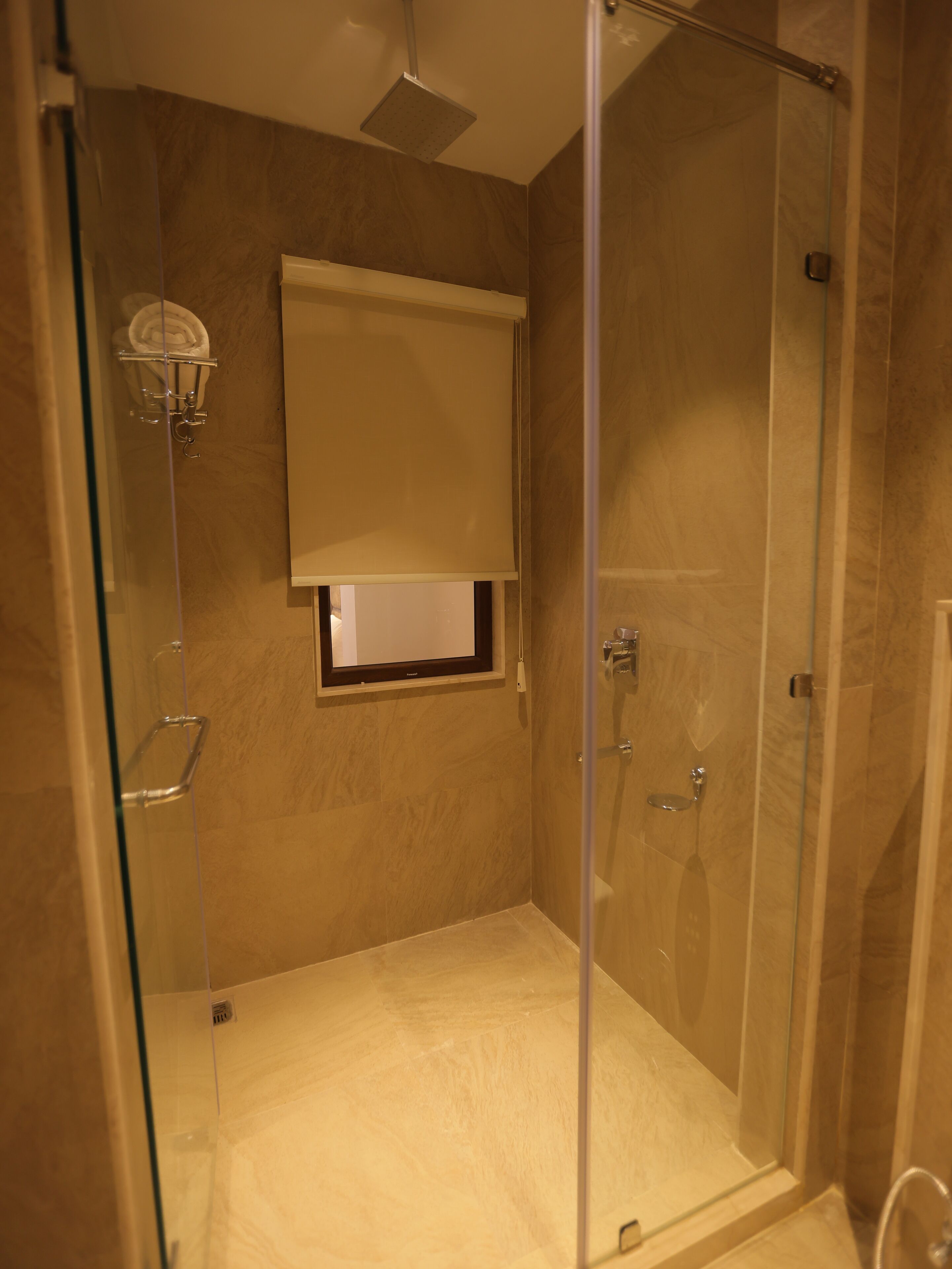 A glass-enclosed shower with a built-in bench, a towel rack, and a window with a blind.