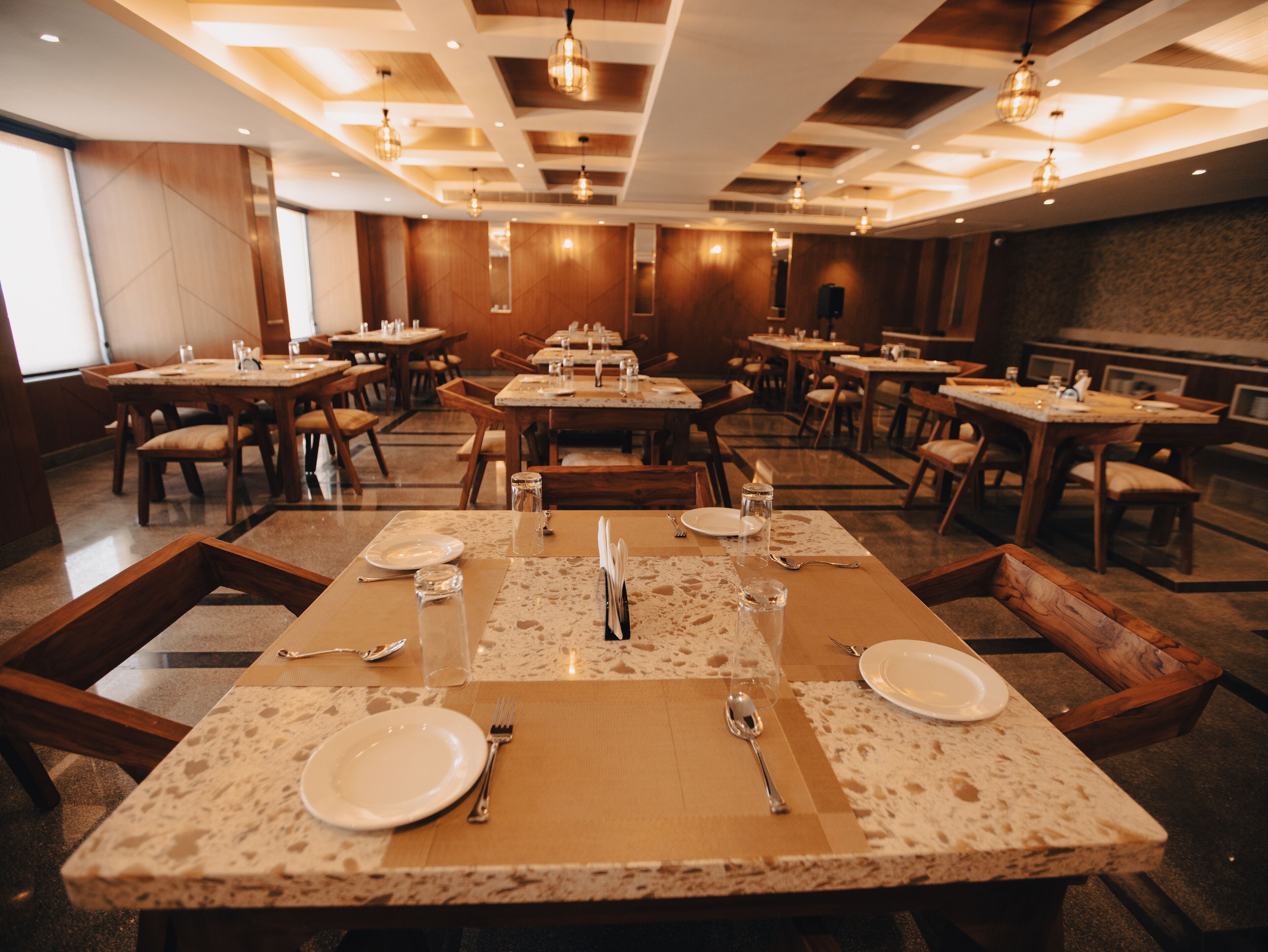 A restaurant with multiple tables set for dining, featuring a mix of wooden and marble tables.