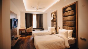 A hotel room with a modern design, featuring two beds, a desk, a chair, a flat-screen TV mounted on the wall, and a ceiling fan. - Clarks Inn Express Dehradun  (Dehradun)