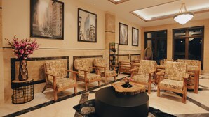 A lobby with wooden chairs, a black ottoman, and a vase of flowers. - Clarks Inn Express Dehradun  (Dehradun)