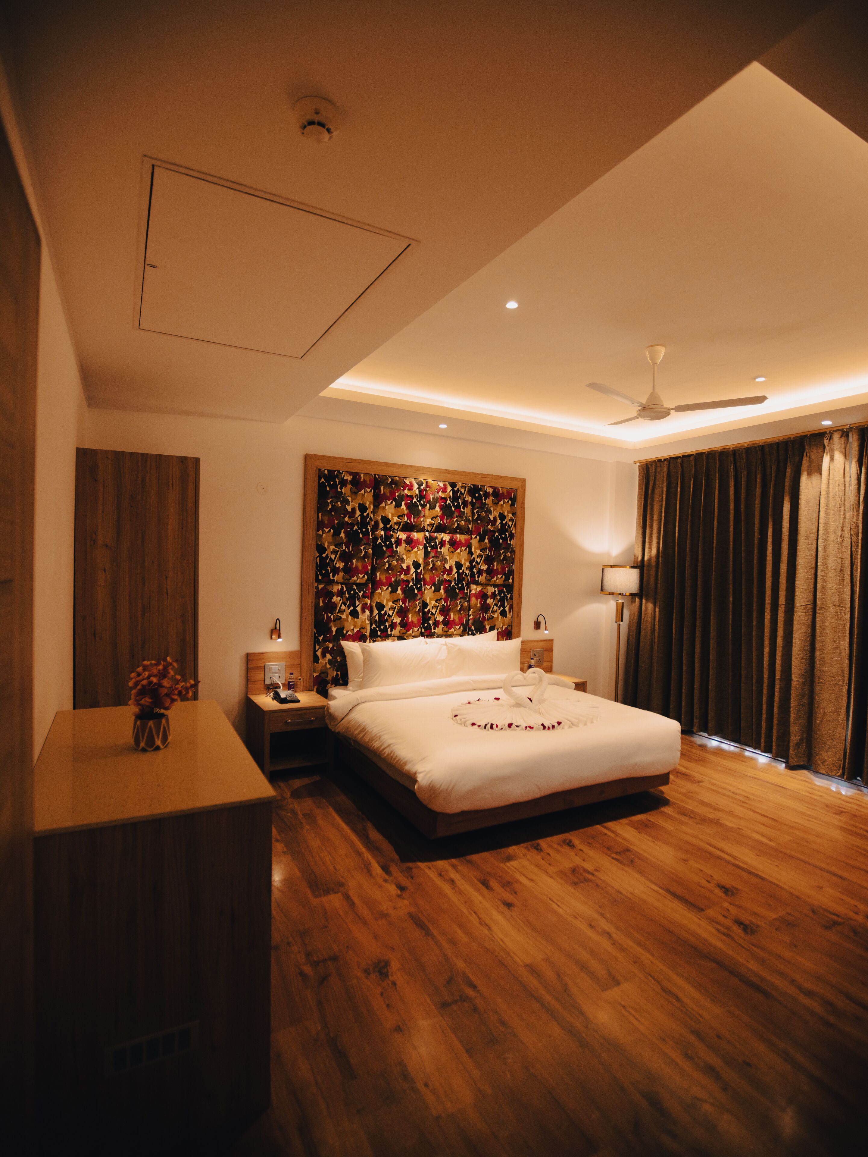 Een moderne slaapkamer met een houten vloer, een groot bed met witte lakens, een plafondventilator en een decoratief wandpaneel.