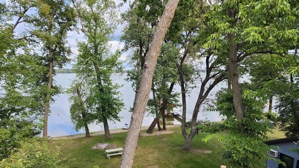 Een terras met een hekwerk dat uitkijkt over een gazon met bomen en een waterpartij.