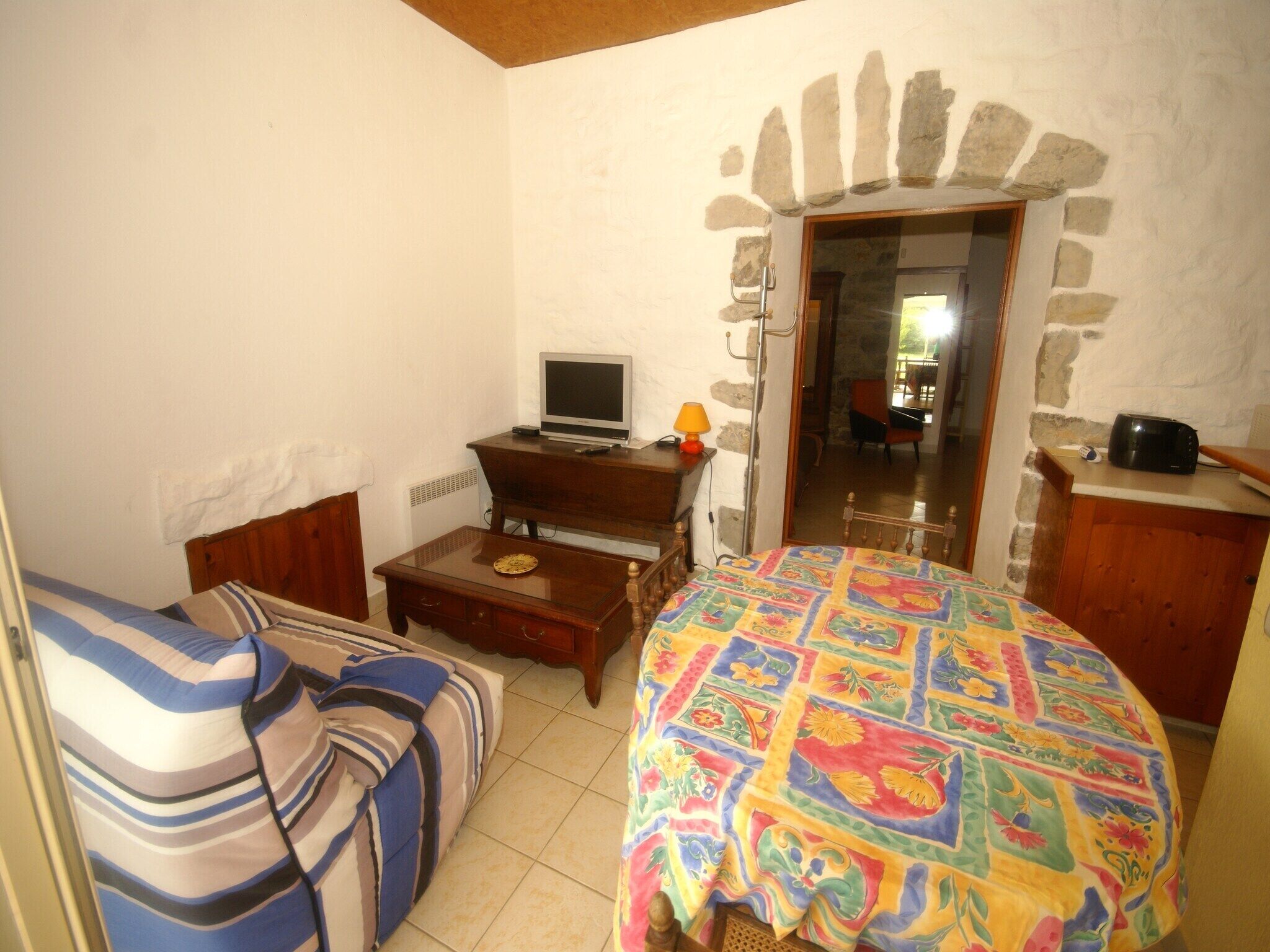 A cozy room with a bed, a desk with a computer, a chair, and a small table with a lamp.