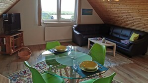 A cozy living room with a glass dining table, green chairs, a black leather sofa, and a television on a wooden stand. - Tranquil Waterside Hideaway (Usedom)