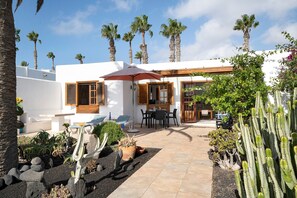 A white building with a patio area, outdoor seating, and cacti.