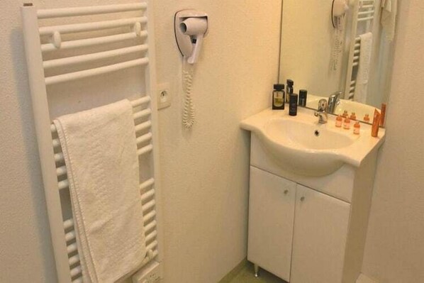 Une salle de bain avec un lavabo blanc, un miroir, un porte-serviettes et un sèche-cheveux.