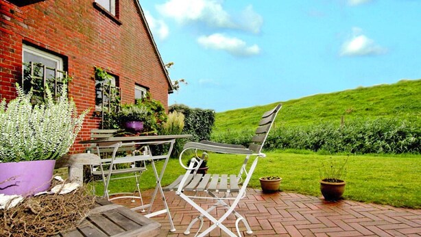 A patio with a table and chairs, a brick wall, and a green lawn. - Ferienwohnung Kapitänskajute, Dornumersiel (Dornumersiel)