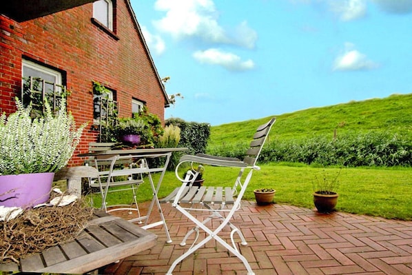 A patio with a table and chairs, a brick wall, and a green lawn. - Ferienwohnung Kapitänskajute, Dornumersiel (Dornumersiel)