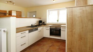 Una cocina con armarios blancos, estufa, lavamanos y ventana con una planta.