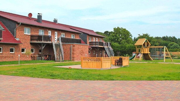Un edificio de ladrillo con techo rojo, una estructura de juego de madera y un camino de ladrillo.