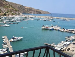 A marina with numerous boats docked, a clear sky, and a hilly landscape in the background.