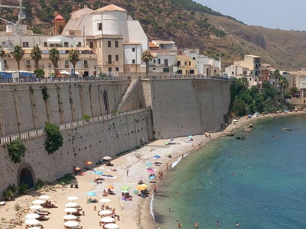 A coastal town with a beach, a stone wall, and buildings in the background.