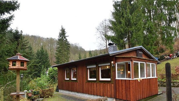 Une cabane en bois avec un porche, une mangeoire à oiseaux et un mur en pierre.