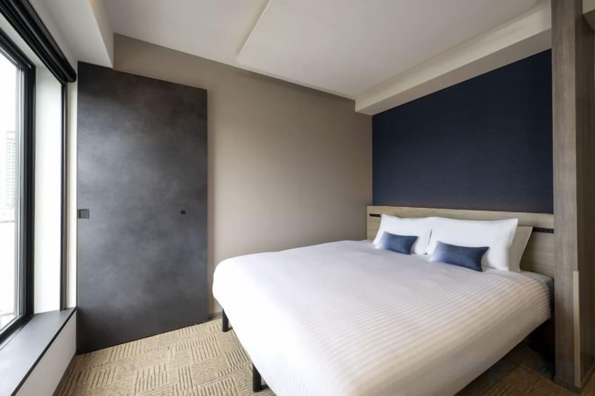 Una habitación de hotel con una cama grande, un ventanal y una pared de color oscuro.