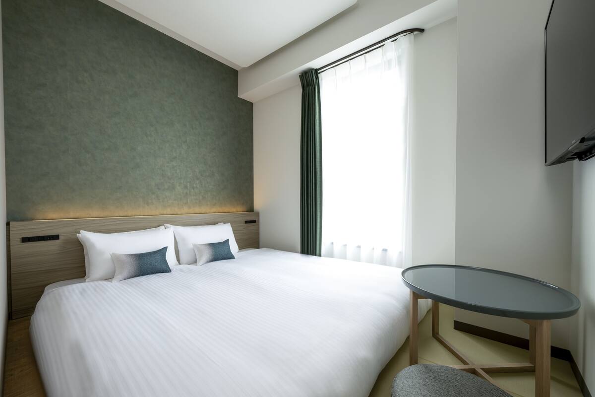 Une chambre d’hôtel avec un grand lit, une petite table ronde et un téléviseur fixé au mur.