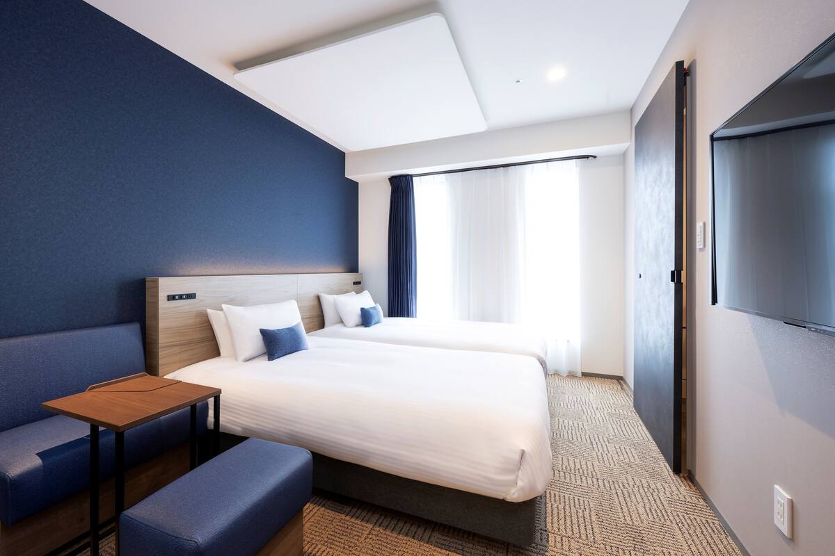 Une chambre d’hôtel moderne avec deux lits, un coin salon et une grande fenêtre.