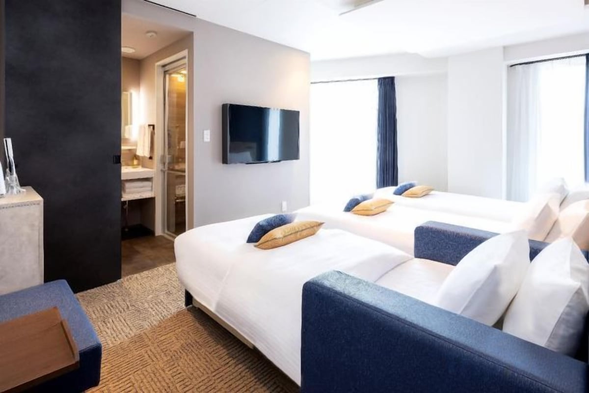 Habitación de hotel con dos camas, televisión y vista al exterior.