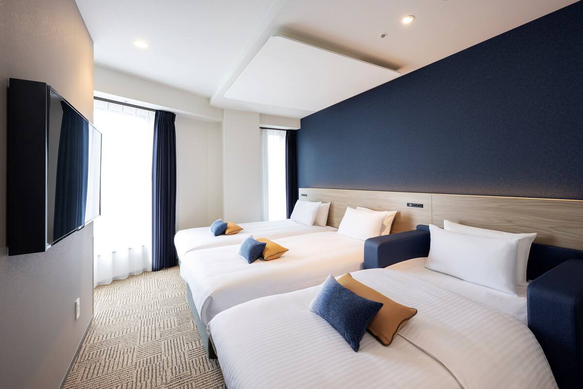 Une chambre d’hôtel avec trois lits, un téléviseur à écran plat, une grande fenêtre avec des rideaux et un design moderne au niveau du plafond.