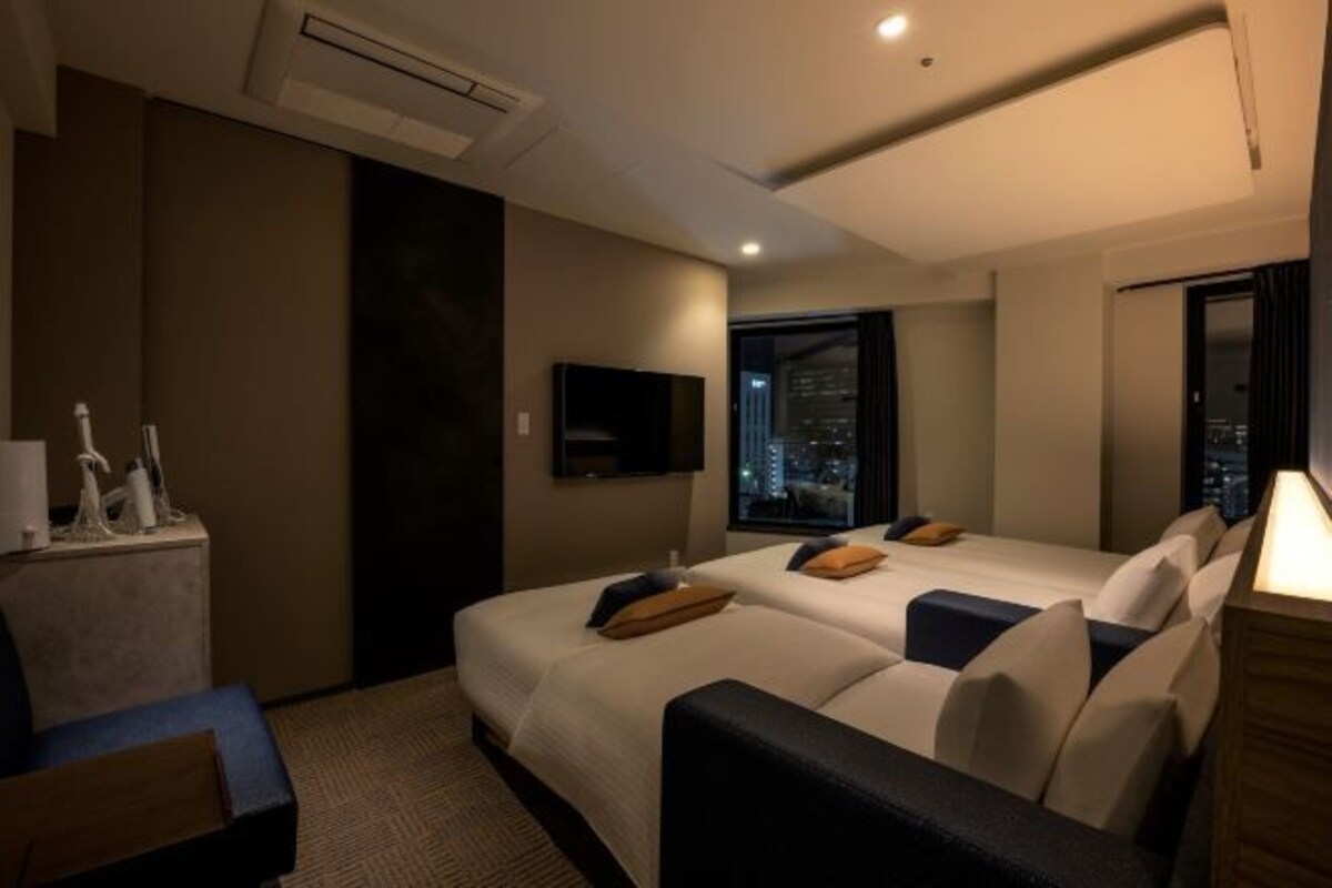 Hotelkamer met twee bedden, een televisie, een raam met uitzicht op de stad en een bureau met toiletartikelen.