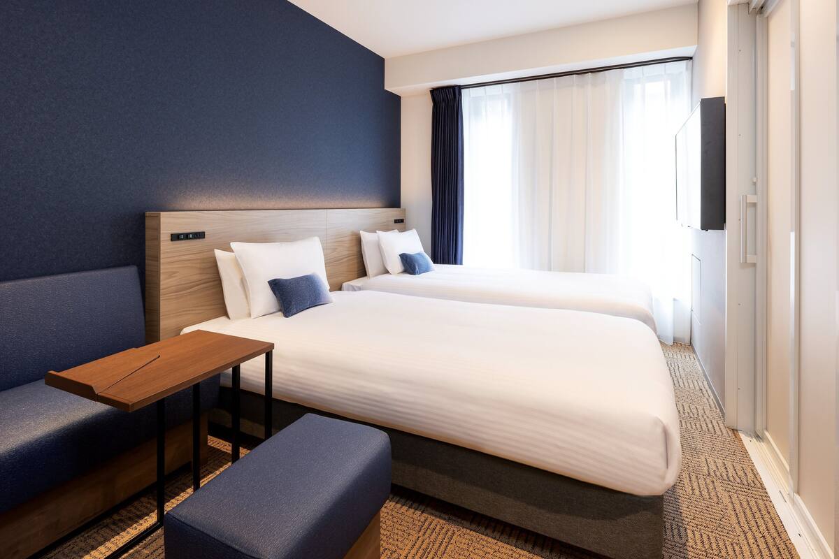 Une chambre d’hôtel avec deux lits, un canapé, une petite table et un téléviseur.