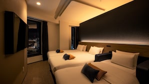 Habitación de hotel con dos camas, un ventanal grande con vista a la ciudad, un televisor de pantalla plana montado en la pared y un cabecero de color oscuro.