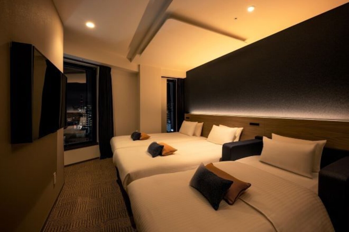 Habitación de hotel con dos camas, un ventanal grande y un televisor de pantalla plana en la pared.