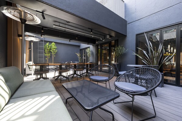 Ein Außenbereich mit Terrasse, einer Sitzecke, Tischen und einer Bar mit Sitzplätzen.