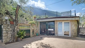 A stone building with a welcome sign, a glass door entrance, and a view of mountains. - Apartment 'Assenza 9' with Lake View, Wi-Fi and Air Conditioning (Brenzone sul Garda)