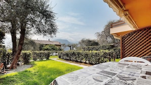 A garden with a table covered in a patterned tablecloth, a white chair, and a view of a mountain in the background. - Apartment 'Assenza 9' with Lake View, Wi-Fi and Air Conditioning (Brenzone sul Garda)