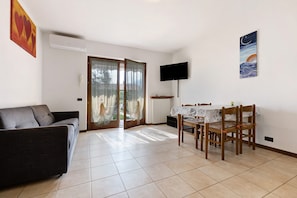 Una sala de estar con un sofá, una mesa de comedor con sillas, un televisor de pantalla plana y un cuadro en la pared.
