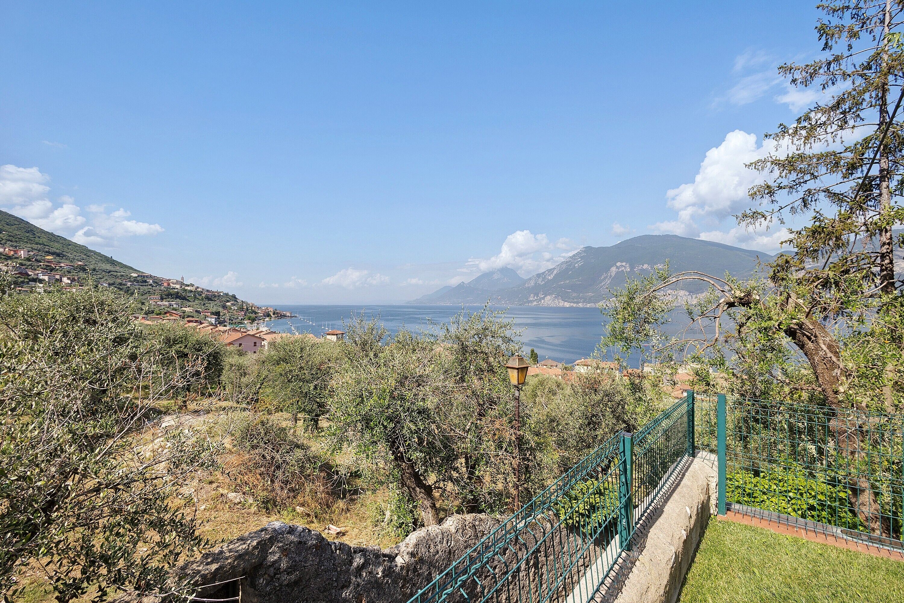 A coastal landscape with a view of the sea, a mountain range, and a green fence.