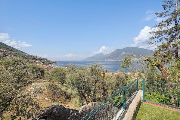 A coastal landscape with a view of the sea, a mountain range, and a green fence.