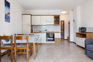 Una cocina compacta con armarios blancos, horno empotrado y comedor con sillas de madera.