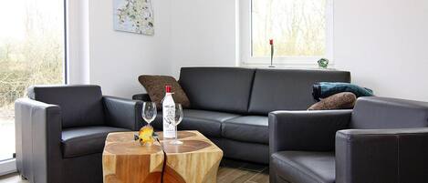 A modern living room with a sectional sofa, a wooden coffee table, and a large window with a view of trees.