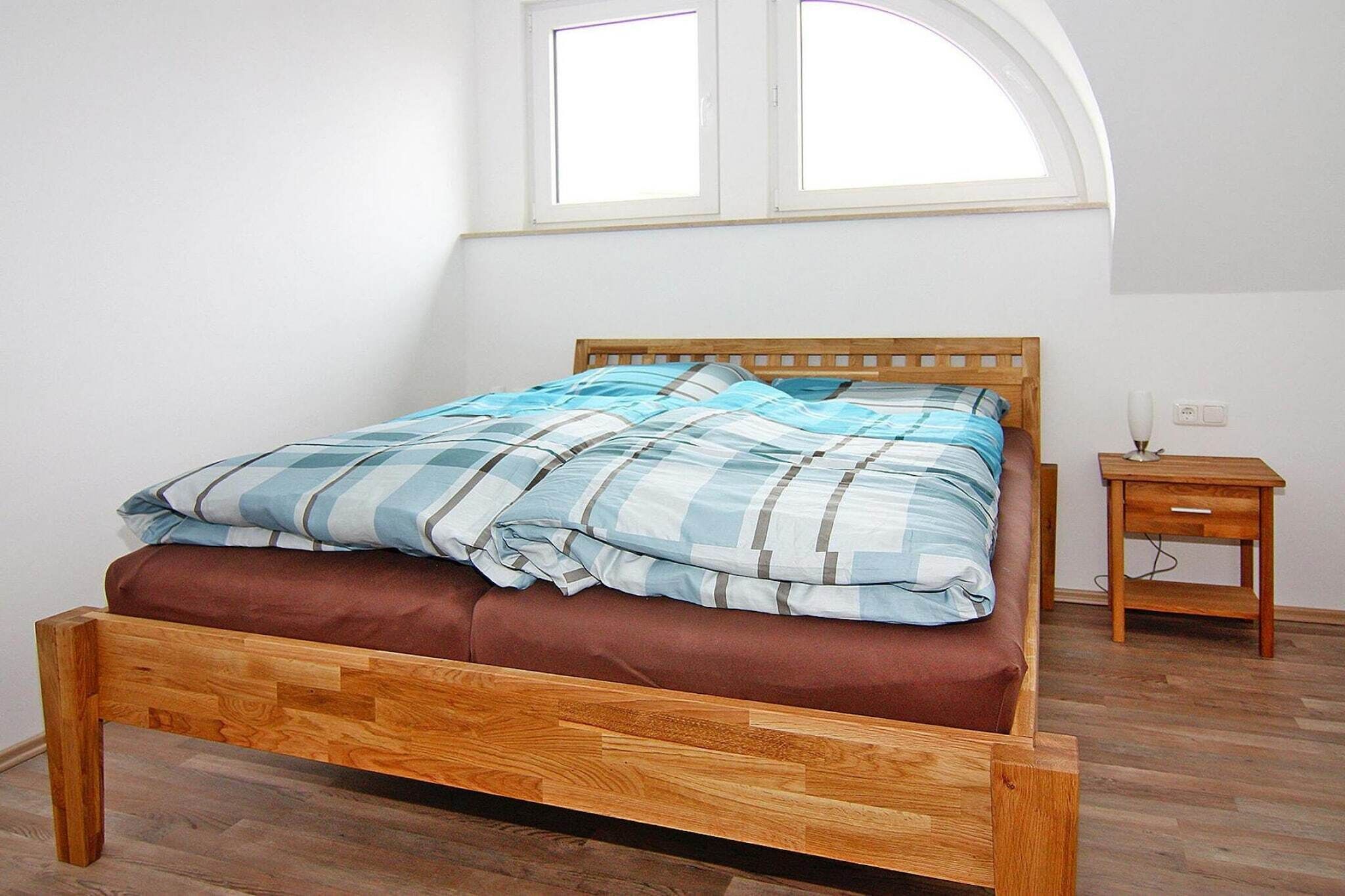 A bed with a wooden frame and a brown mattress, a bedside table, and a window above the bed.