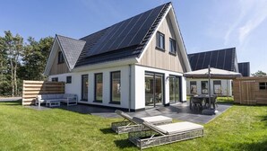 Een modern huis met een schuin dak, grote ramen en een terras met buitenmeubilair.
