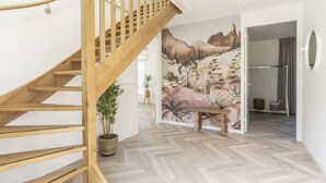 Een houten trap die leidt naar een kamer met een woestijnmotief op de muur, een potplant en een bank.