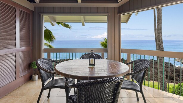 A round table with wicker chairs and a candle on a balcony with a view of the ocean. - Aloha Condos, Kanaloa at Kona, Condo 2906, Oceanfront, AC (Kailua Kona)