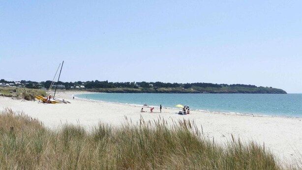 En strand med en sejlbåd, folk der slapper af, og en fjern, grøn bakke.