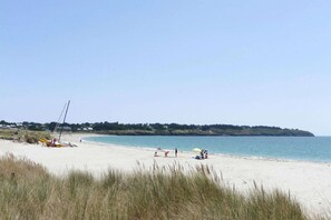 A beach with a sailboat, people relaxing, and a distant green hill.