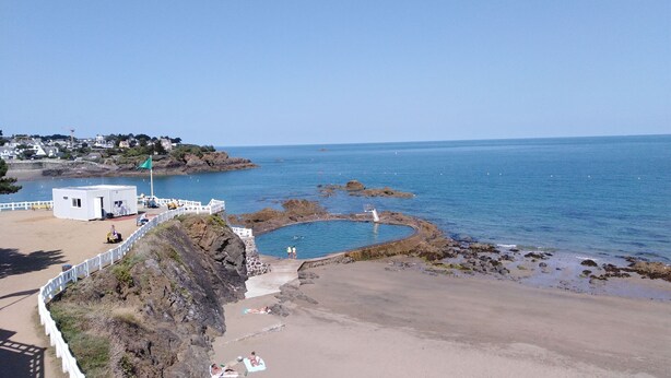 Una playa costera con piscina, una torre de salvavidas y un edificio blanco.