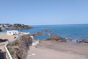 A coastal beach with a swimming pool, a lifeguard tower, and a white building.